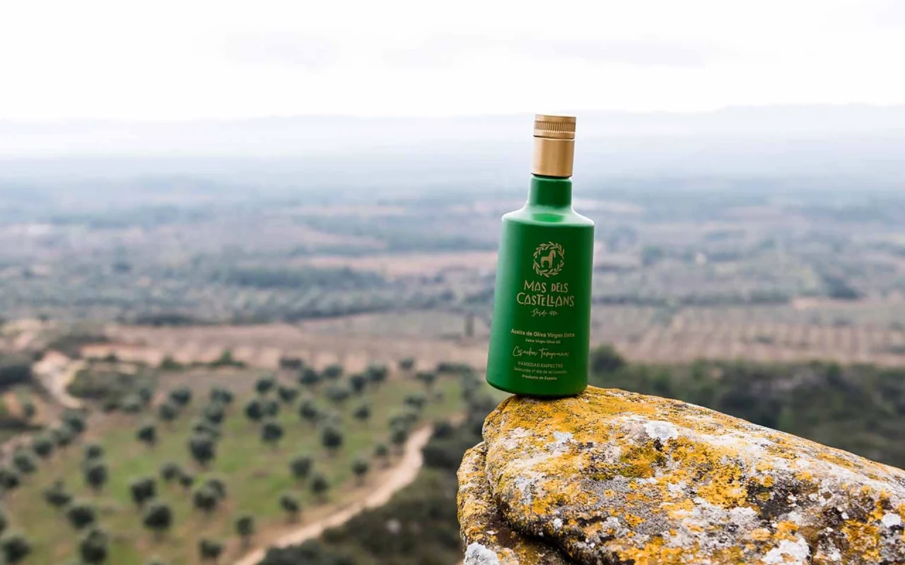 botella de aceite de oliva de Mas dels Castellans con el paisaje del Matarraña